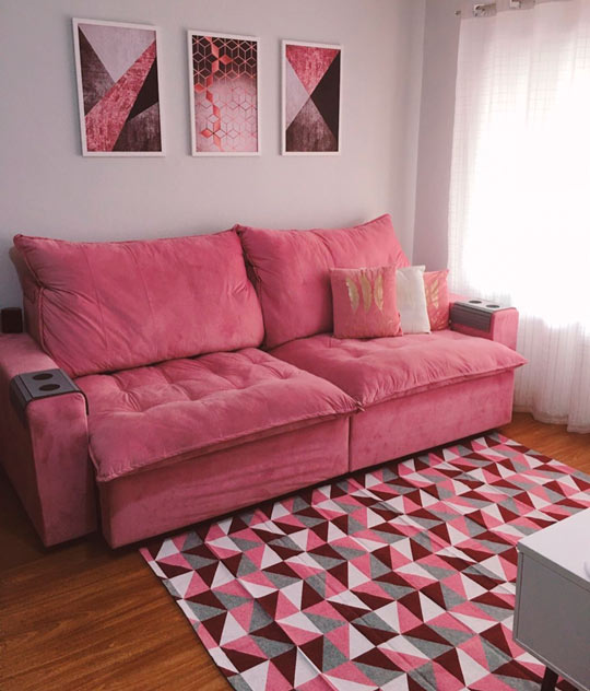 sofá retrátil rosa com tapete geométrico rosa e conjunto de quadros cor de rosa na parede