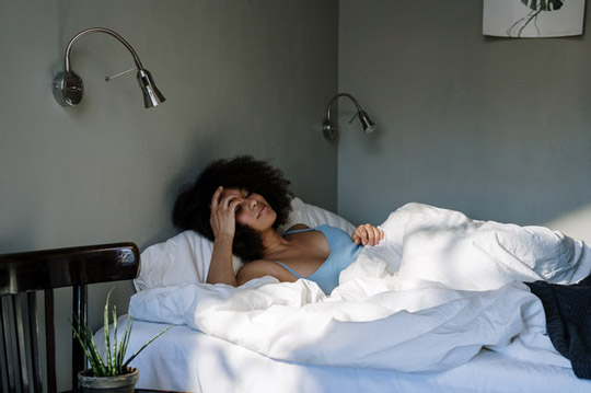 mulher deitada na cama relaxando por ter uma cortina para quarto que corta a luz e beneficia seu descanso