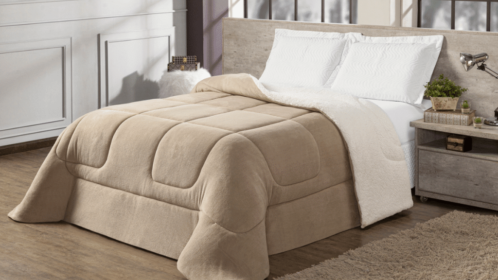 Cama de casal com coberdrom bege de tecido macio e forro sherpa branco, ambiente clean com cabeceira de madeira clara e tapete felpudo.