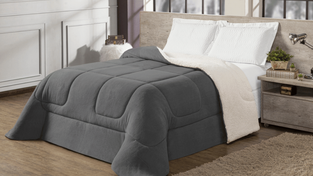 Cama de casal com coberdrom cinza escuro de toque aveludado e verso sherpa branco, cabeceira rústica e decoração neutra ao redor.