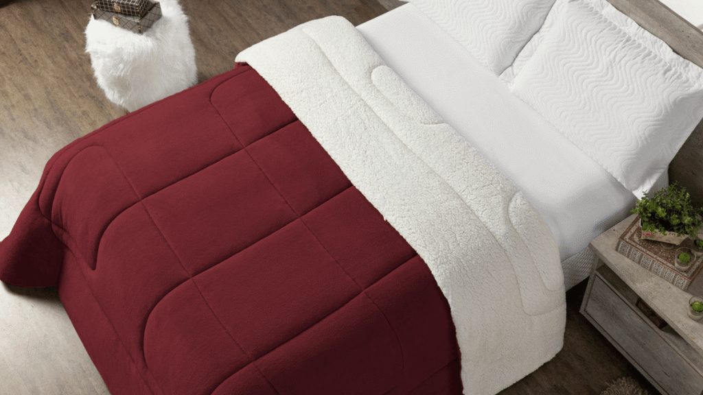 Cama de casal vista aérea, coberta por coberdrom vermelho intenso e forro sherpa off-white, destacando textura acolchoada.