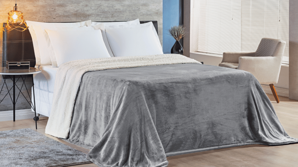 Cobertor Alaska cinza médio com interior de pelúcia branca posicionado sobre cama em um quarto com decoração neutra.